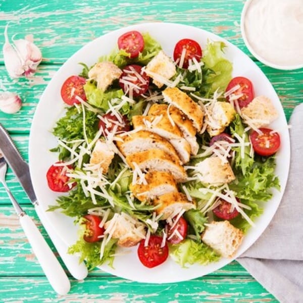 A Caesar salad with grilled chicken, croutons, cherry tomatoes, and shredded cheese.