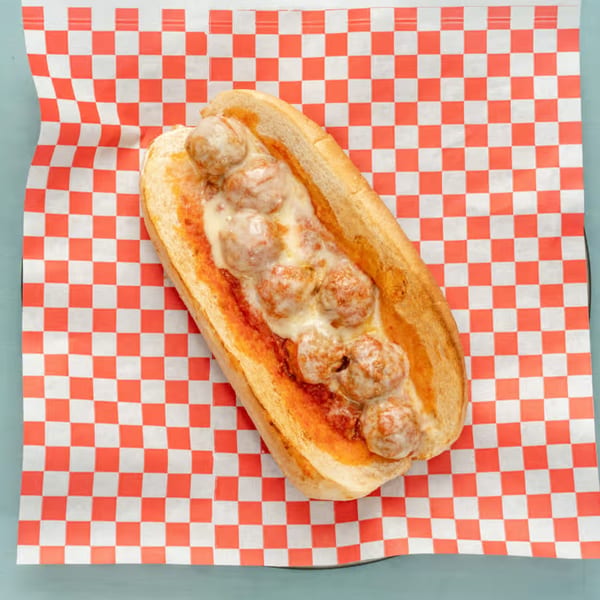 Meatball sub sandwich with melted cheese and red sauce on a red and white checkered paper.