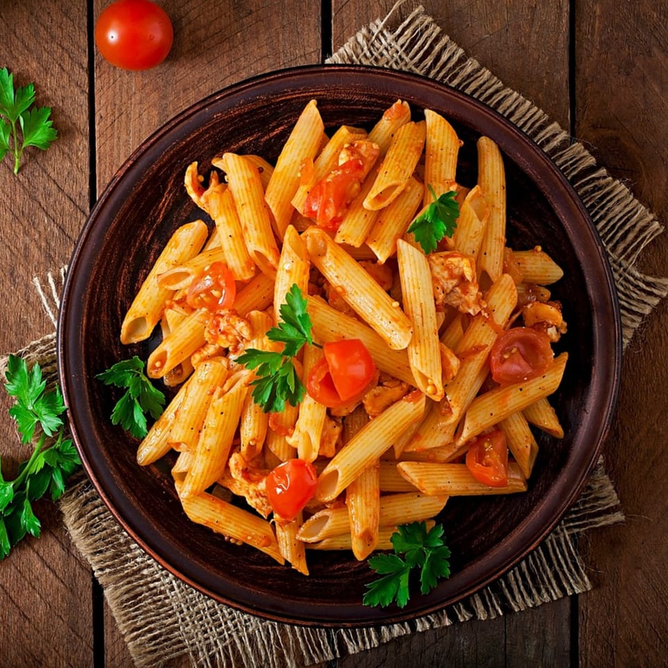 Penne pasta with tomato sauce, chicken, and fresh parsley on a rustic wooden table.
