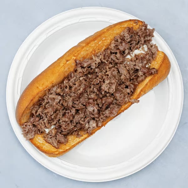 A large cheesesteak sandwich with shredded meat and melted cheese on a white plate.