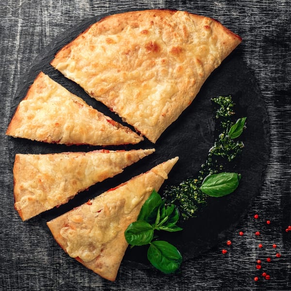 Slices of golden-brown calzone with melted cheese, served on a dark plate with pesto and basil.